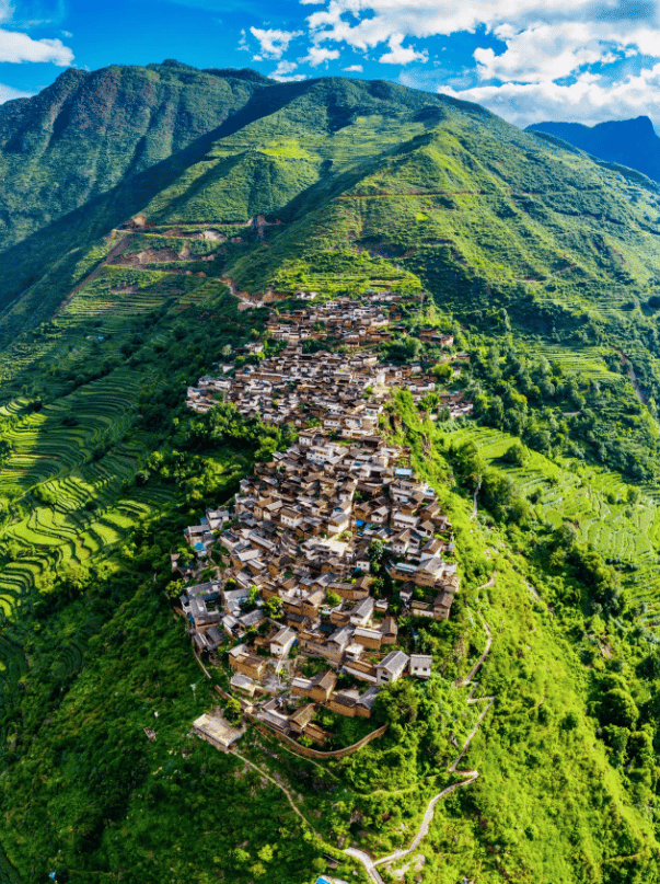 Aerial view of a traditional stone mountain village surrounded by lush green terraced rice fields.