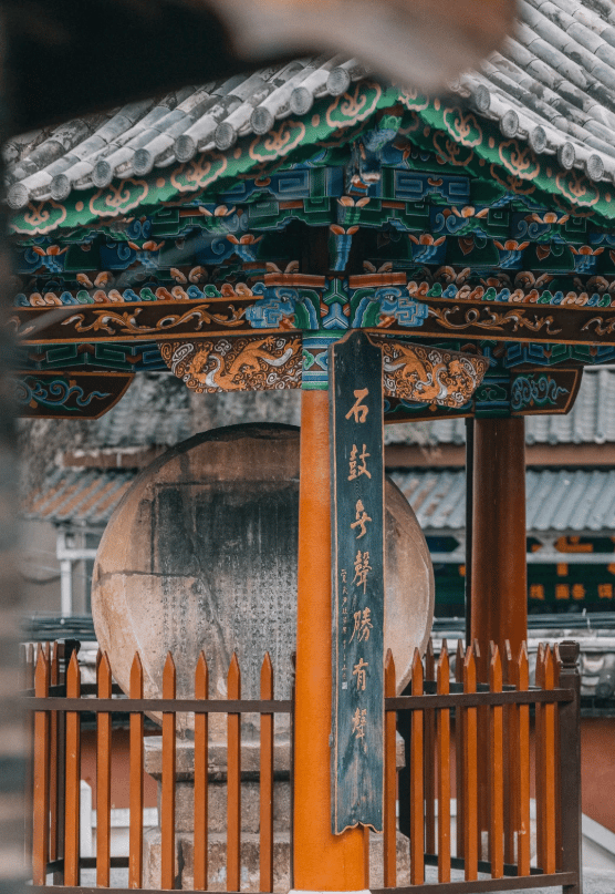 Ornate Chinese temple architecture featuring a stone drum and calligraphy inside a colorful pavilion.