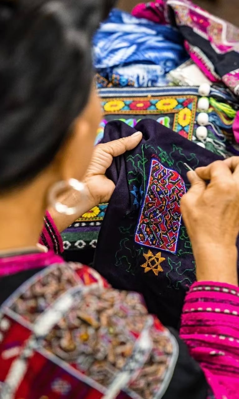 Close-up of an artisan hand-stitching intricate traditional Hmong embroidery on black fabric.