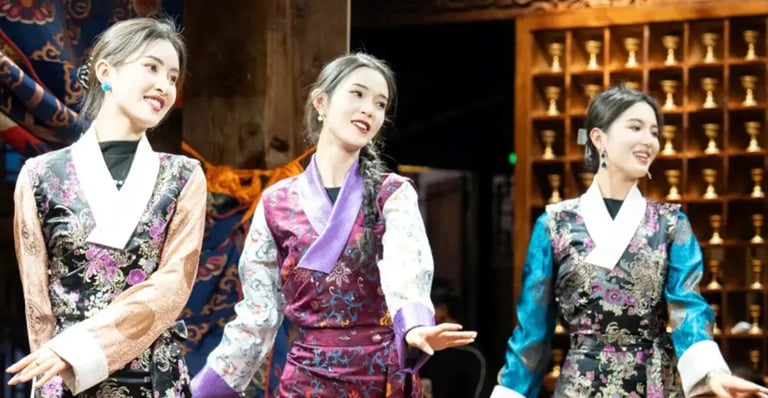 Three women in traditional Tibetan silk dresses perform a cultural dance on a stage.