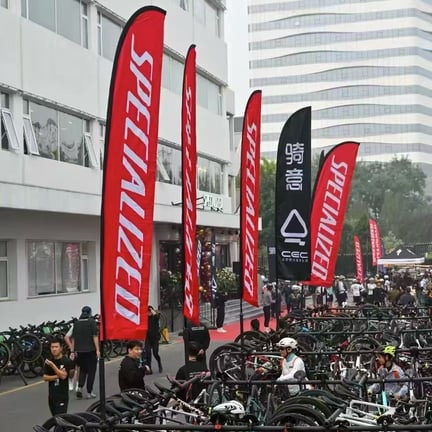 Red Specialized feather flags stand tall above rows of parked bicycles at an outdoor cycling event.