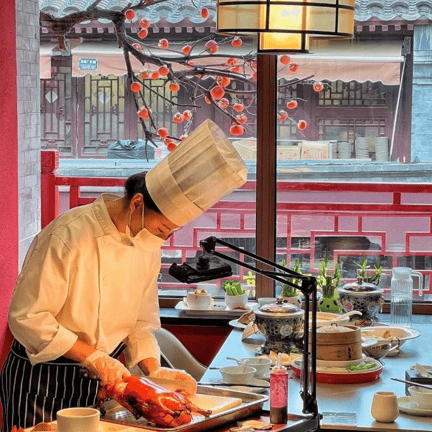 A chef in a white uniform carves a traditional roasted Peking duck at a restaurant table.