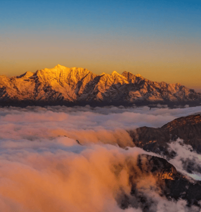 Golden sunrise over snow-capped mountain peaks rising above a thick sea of pink and white clouds.