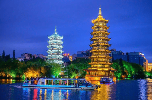 Illuminated Sun and Moon Pagodas reflecting on Shanhu Lake with a tour boat in Guilin, China at night.