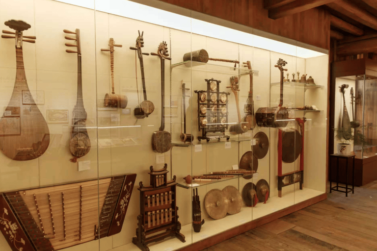 Collection of traditional Chinese musical instruments like the pipa, erhu, and gongs in a museum display case.