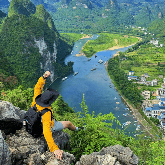 A hiker overlooks the Li River and limestone karst mountains in Guilin, China, from a rocky summit.