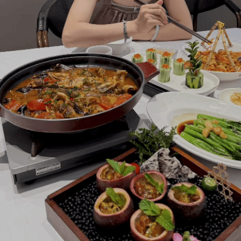 A person using chopsticks to eat authentic Chinese cuisine including spicy braised fish, bok choy, and passion fruit