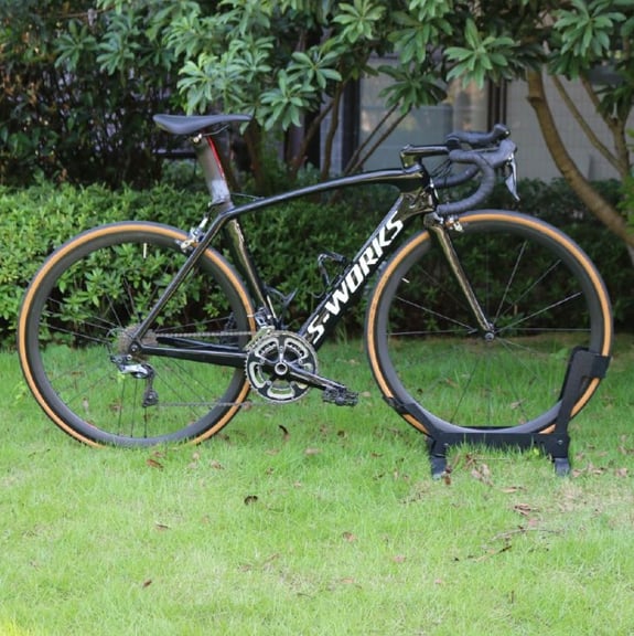A black Specialized S-Works Venge carbon fiber road bike with tan wall tires parked on a green lawn.