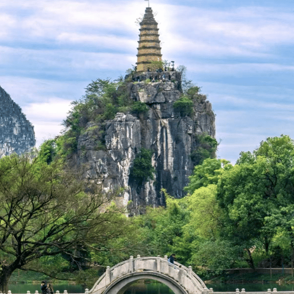Ancient stone pagoda atop a rocky limestone peak in Guilin, China, overlooking a traditional arched stone bridge.