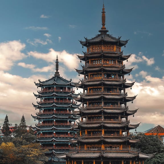 Traditional multi-tiered Sun and Moon Pagodas in Guilin, China under a cloudy blue sky.