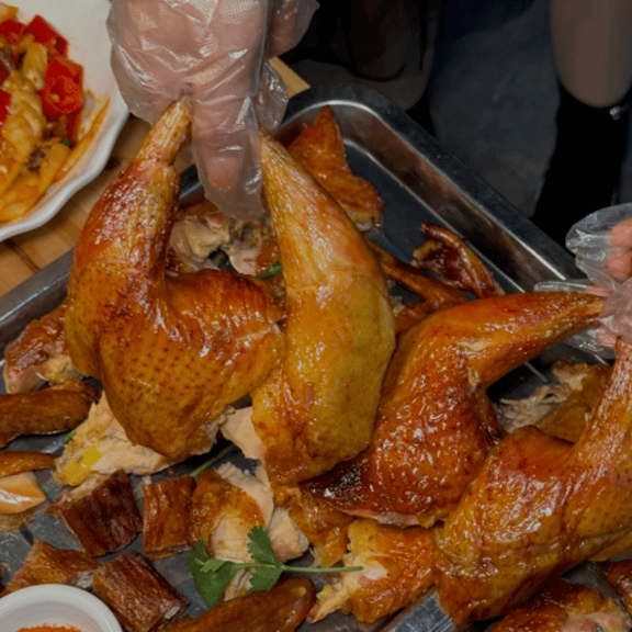 A person wearing plastic gloves holds up a crispy roasted whole chicken leg over a metal platter.