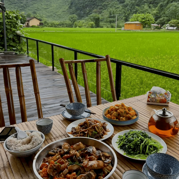A traditional dinner served on a bamboo table overlooking lush green rice fields in a rural valley.