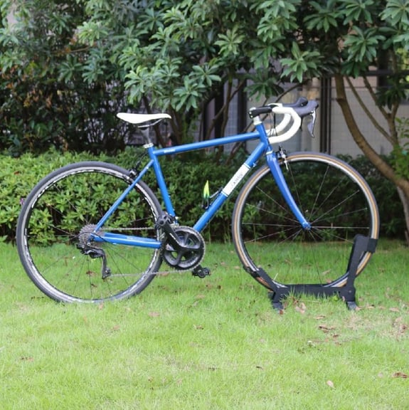 A retro pink road bike with white drop handlebars parked on a green grass lawn.
