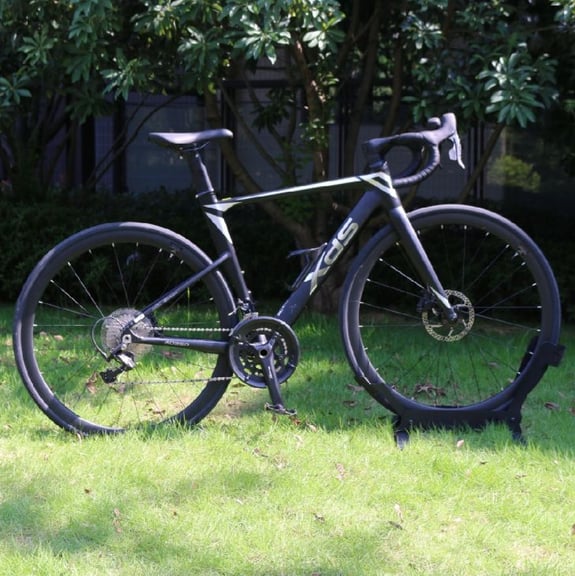 A black XDS road bike with disc brakes parked on a green lawn with a garden background.