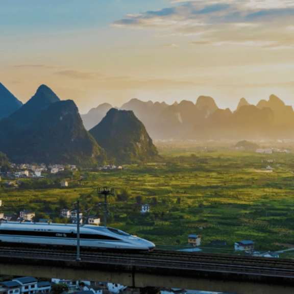 A high-speed train travels across a bridge with a backdrop of karst mountains at sunset in China.
