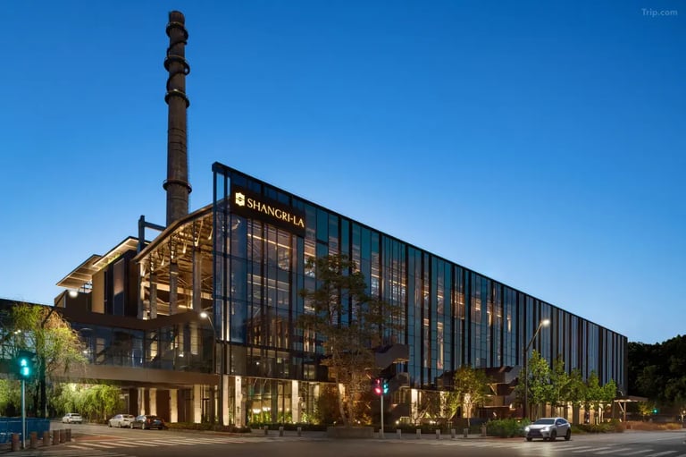 The modern glass exterior of the Shangri-La Shougang Park hotel in Beijing at twilight with industrial chimney.