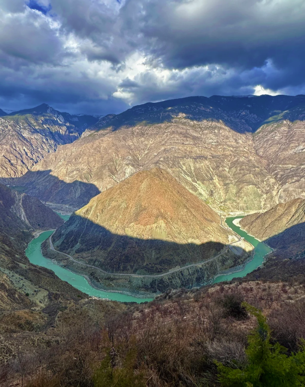 Panoramic view of the First Bend of the Yangtze River winding through a deep mountain valley under a cloudy sky.