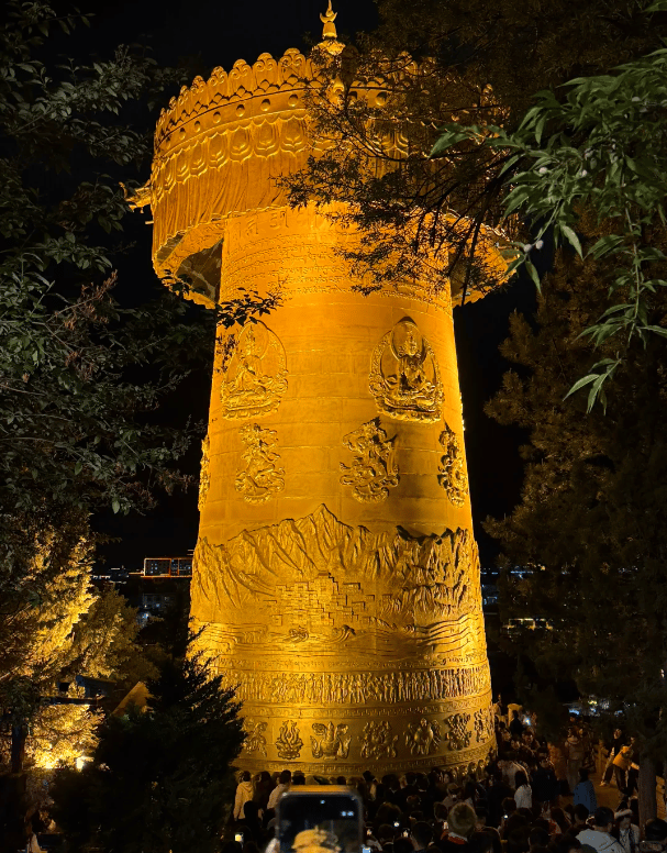 Illuminated golden giant prayer wheel in Shangri-La, China at night with intricate carvings.