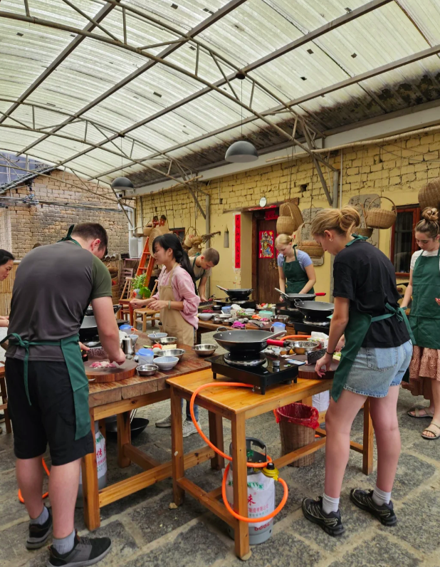 Students prepare traditional recipes in an outdoor Chinese cooking class with woks and fresh ingredients.